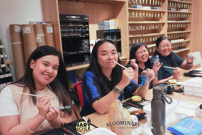 Four painters smiling at the workshop table with their BINI figurines