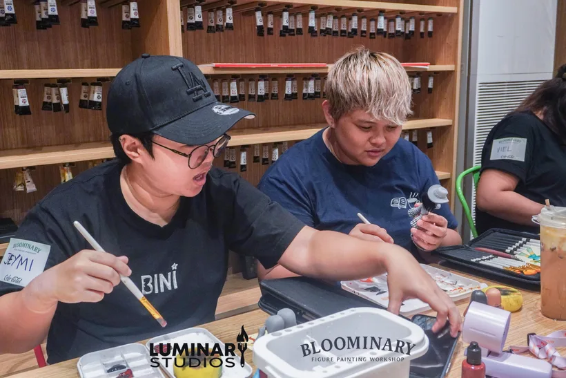 Two painters applying fine details to BINI figurines side by side