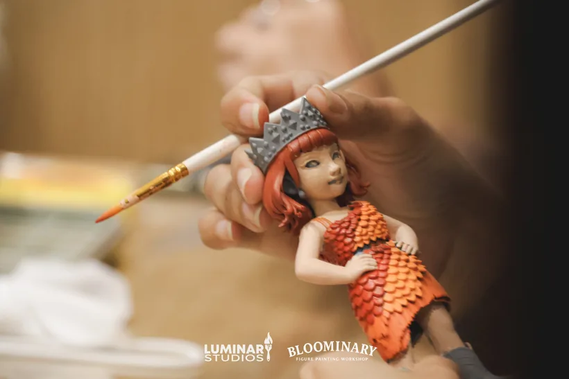 Finished hand-painted BINI 3D printed figurine held beside fine-tip paintbrush